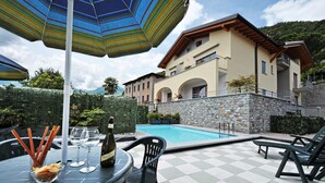 A poolside area with a checkered floor, outdoor seating, and a large umbrella. - Residenza Bel Sit - Apt. 6 (Domaso)