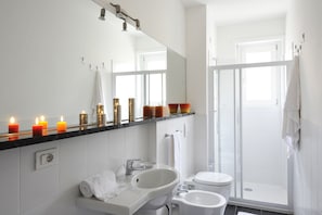 A modern bathroom with a white sink, mirror, and toilet. There are candles on the vanity and a shower door visible. - Residenza Bel Sit - Apt. 6 (Domaso)