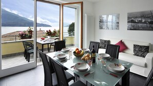 A dining area with a glass table, chairs, and a view of a lake and mountains. - Residenza Bel Sit - Apt. 6 (Domaso)