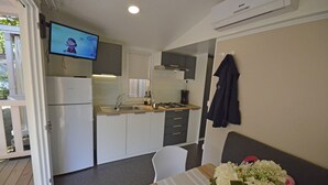 A compact kitchen with a refrigerator, stove, sink, and a flat-screen TV mounted above the counter. - TopCamp in Union Lido (Cavallino-Treporti)