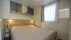 A neatly arranged hotel room with a large bed, a bedside table with a phone, a mirror above the bed, and a window with curtains. - TopCamp in Union Lido (Cavallino-Treporti)