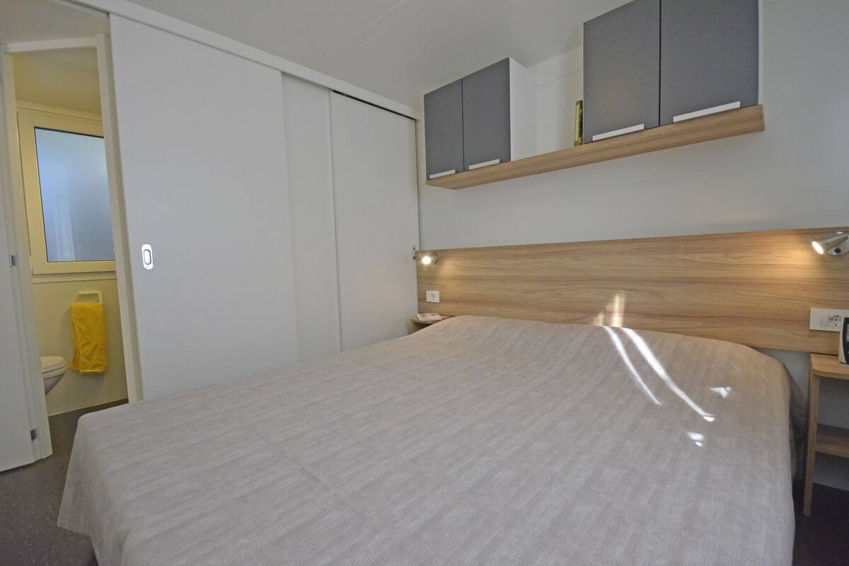 A bedroom with a bed, a wooden headboard, a bedside table, a nightstand, a mirror, and a wardrobe.
