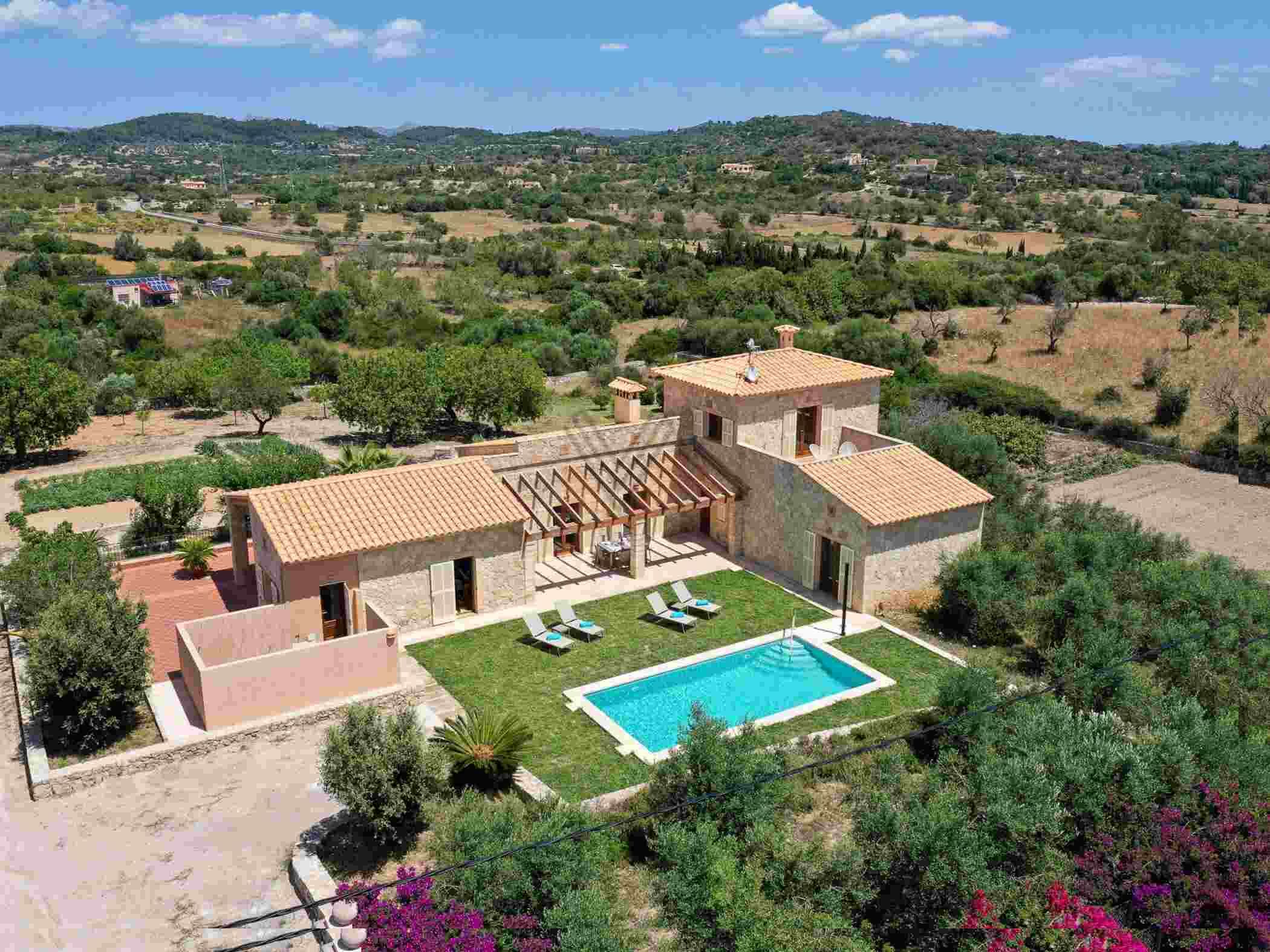 A villa with a swimming pool, a covered patio, and a view of the surrounding countryside.