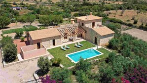 A villa with a swimming pool, a covered patio, and a view of the surrounding countryside.