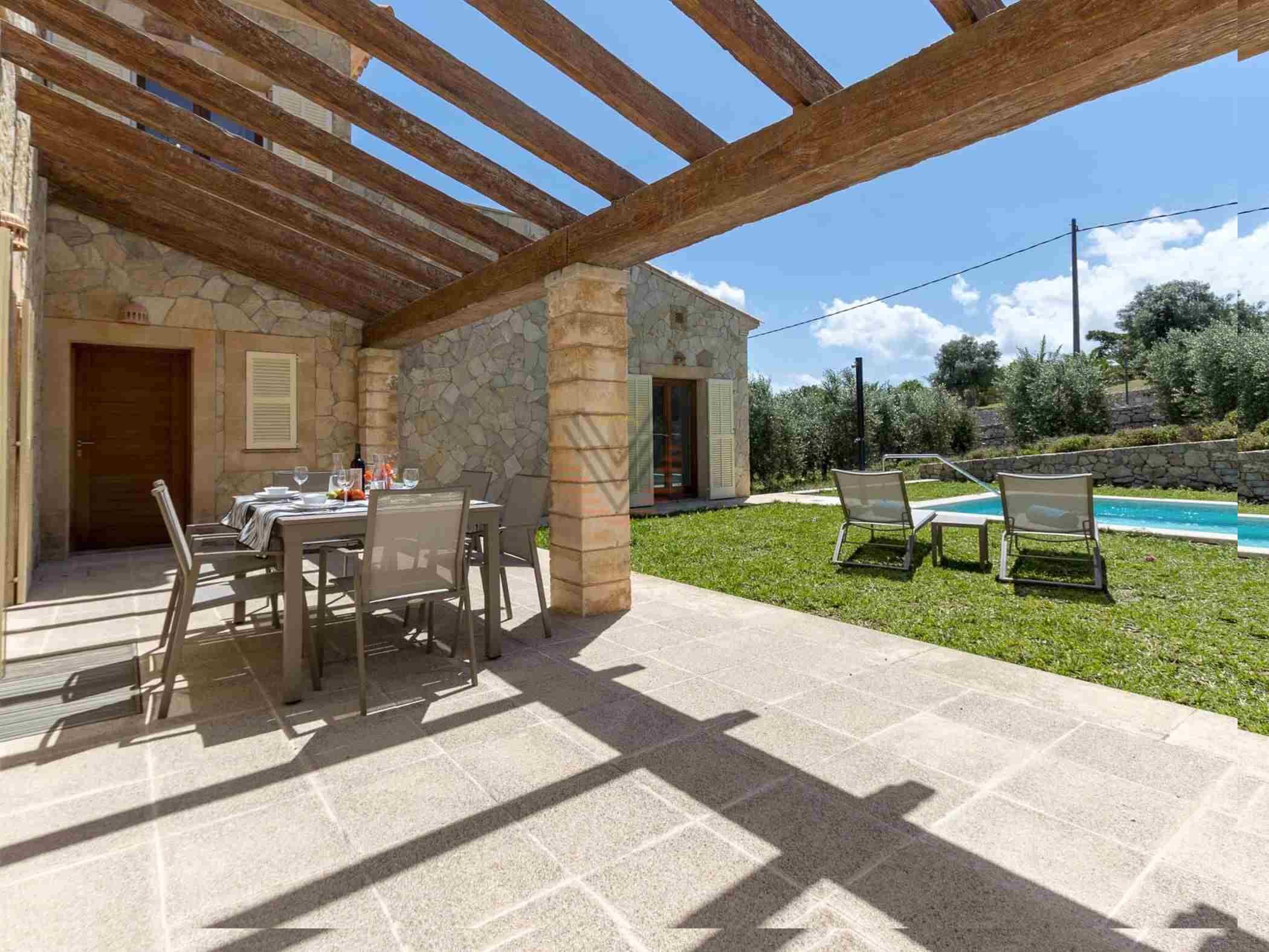 A covered outdoor dining area with stone walls and a pool in the background.