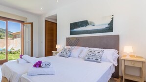 A hotel room with a large bed, two bedside tables, a painting on the wall, and a view of the outdoors.