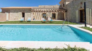 A pool area with a stone building, outdoor seating, and a clear sky.