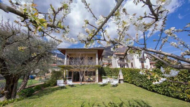 A two-story building with a garden in front, including a lawn and a few trees. - Antico Ulivo (Tremezzina)