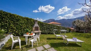 A patio with outdoor furniture, a grill, and a view of mountains. - Antico Ulivo (Tremezzina)