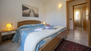 A bedroom with a bed, nightstands, a lamp, a painting, and a door leading to another room. - Antico Ulivo (Tremezzina)