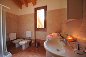 A bathroom with a shower, bidet, toilet, and sink. There are candles on the sink and a window above the toilet. - Vista d'Oro Ulivo Apt. 16 (Perledo)