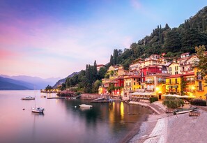 A waterfront town with colorful buildings, boats docked along the shore, and a calm lake.