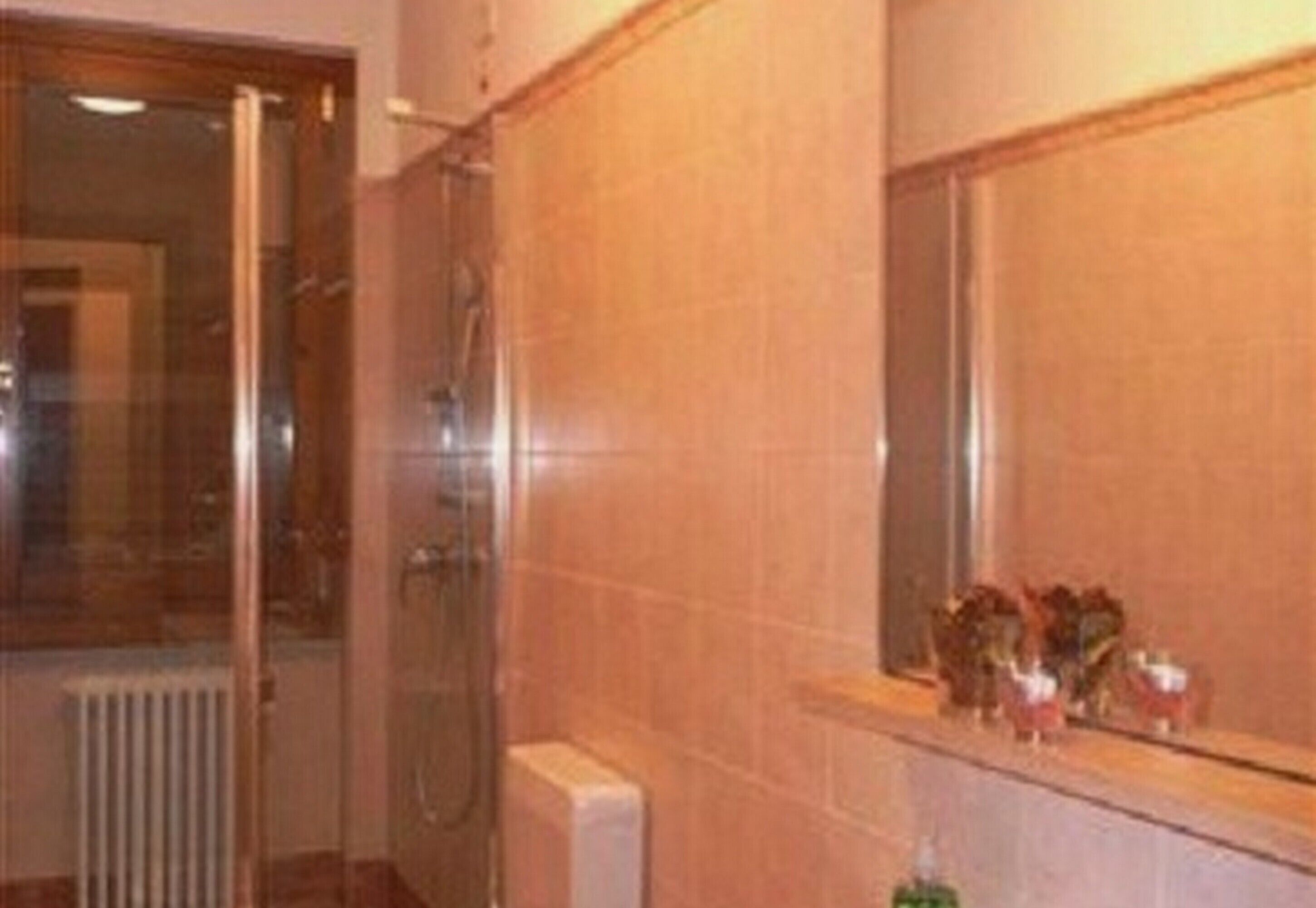 Une salle de bain avec une douche à parois de verre, un mur carrelé et un miroir surmonté d’une étagère.