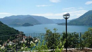 Ein malerischer Blick auf einen See mit Bergen im Hintergrund, einem Metallzaun und einer Straßenlaterne.