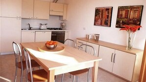 A compact kitchen with a dining table, chairs, and a bowl of fruit. There are cabinets, a stove, and a sink. - Le Vele Terrazzo (San Siro)