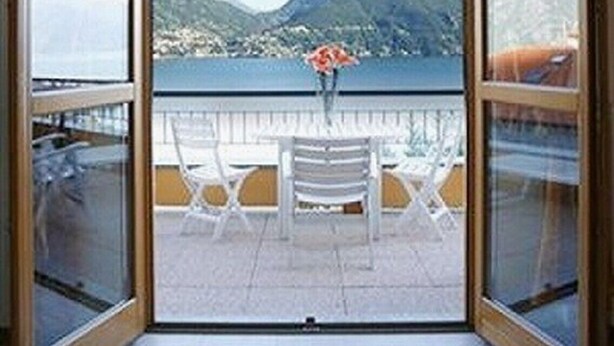 A room with a view of mountains and a body of water through large glass doors. - Le Vele Terrazzo (San Siro)