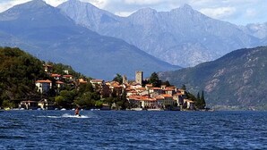A coastal town with buildings on a hillside, a body of water in the foreground, and mountains in the background. - Le Vele Terrazzo (San Siro)