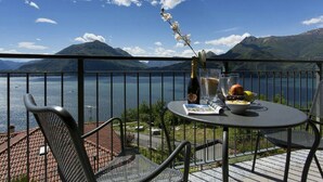 A balcony with a table, chairs, a bottle, and a bowl of fruit. - Vista d'Oro Ulivo Apt. 8 (Perledo)