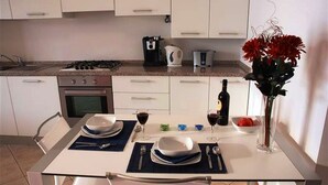 Eine moderne Küche mit weißen Schränken, einem Gasherd, einer Kaffeemaschine und einem Esstisch, gedeckt mit Tellern, Besteck und einer Weinflasche.