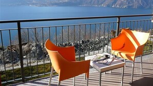 Ein Balkon mit zwei orangefarbenen Stühlen und einem Tisch, mit Blick auf einen See und Berge im Hintergrund.