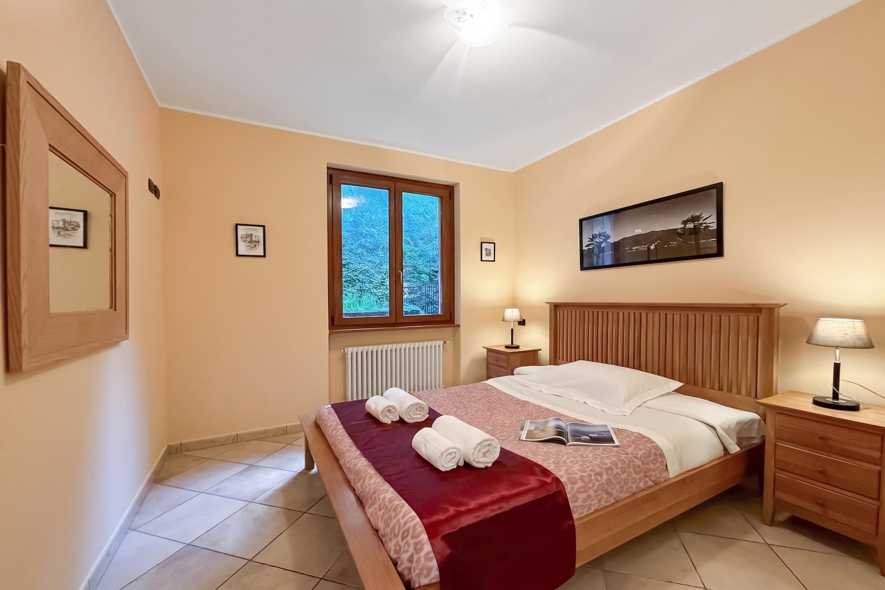 Une chambre à coucher avec un lit, une fenêtre, une table de chevet, une lampe et un tableau encadré au mur.