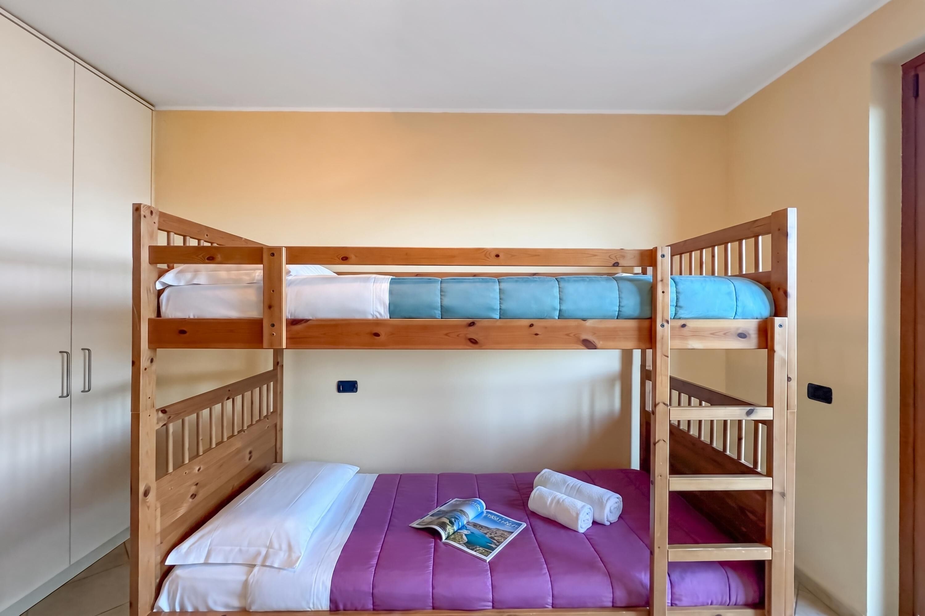 A bunk bed with a purple mattress, a magazine, and rolled towels.