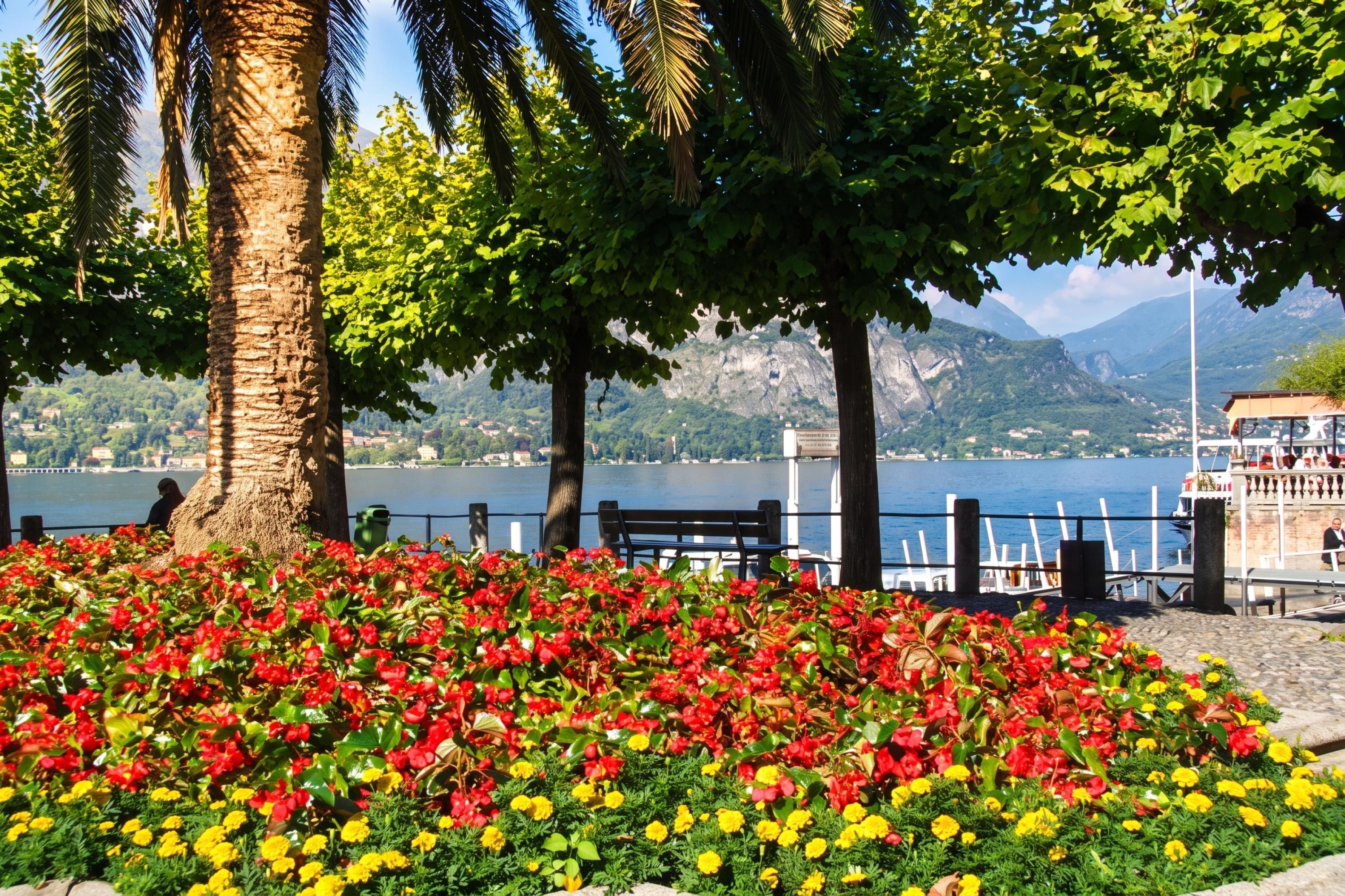 A waterfront park with a flower bed, benches, and a view of a lake and mountains.
