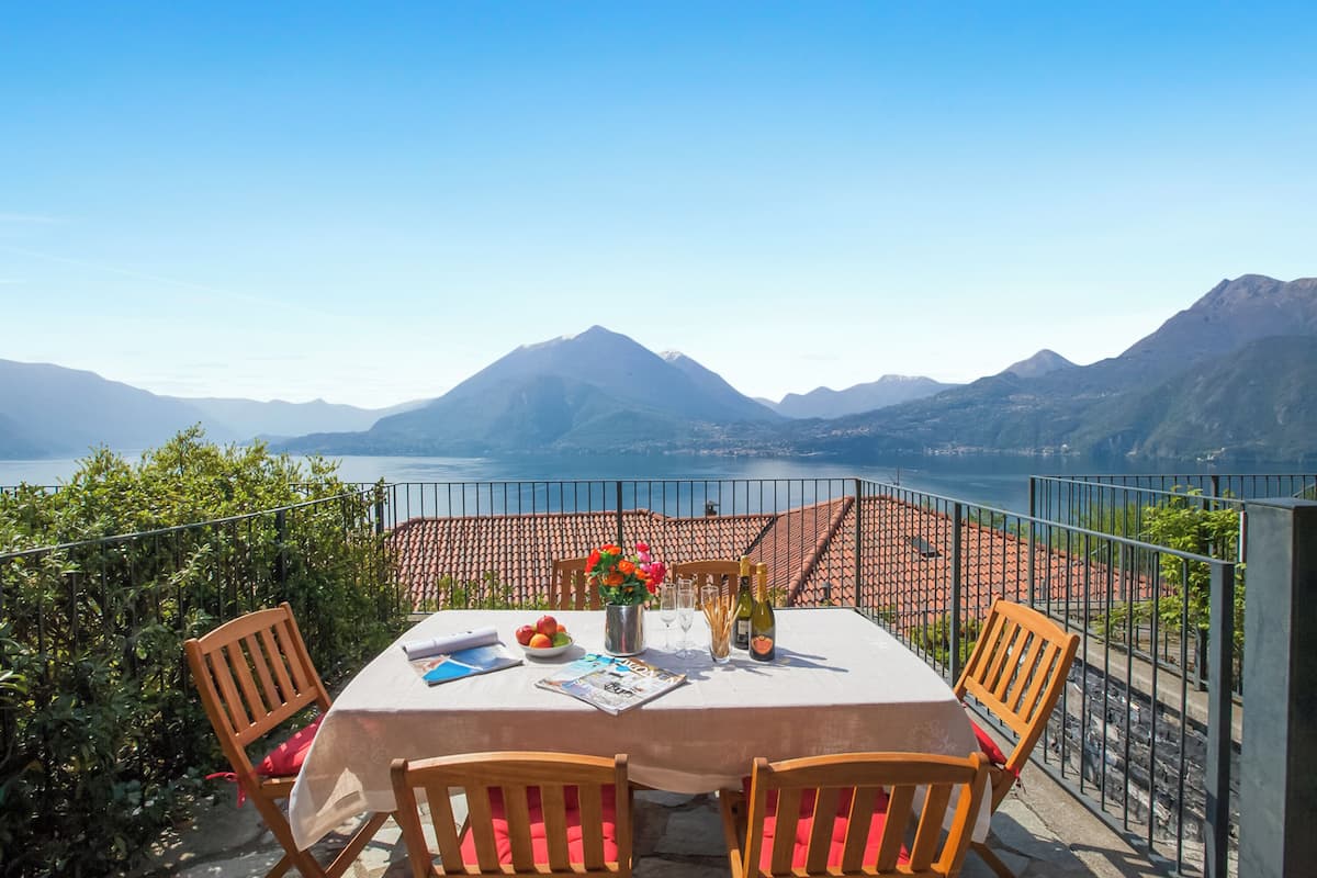 A terrace with a table set for two, overlooking a mountainous landscape and a body of water.