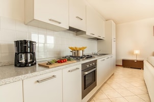 A modern kitchen with white cabinets, a gas stove, a coffee maker, and a cutting board with vegetables.