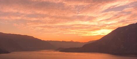 A panoramic view of a lake surrounded by mountains during sunset.