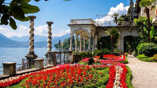 A garden with a pathway, classical columns, and a view of the lake.