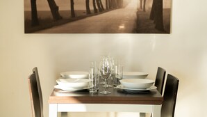 A dining table set with plates, glasses, and cutlery, with a framed picture of a tree-lined path above.