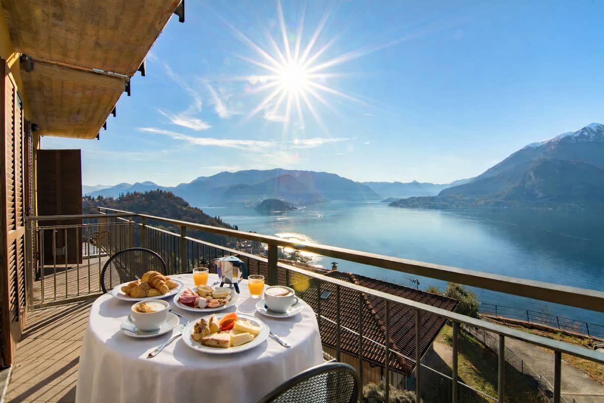 A table set with breakfast items and a scenic view of a lake and mountains.