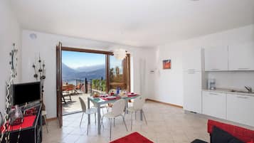 Una sala moderna con alfombra roja, un sofá negro y rojo, un área de comedor con mesa y sillas, y una cocina con armarios blancos.