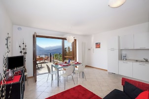 A modern living room with a red rug, a black and red sofa, a dining area with a table and chairs, and a kitchen with white cabinets.