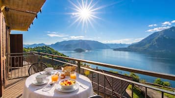 A table set with breakfast items on a balcony overlooking a lake and mountains.