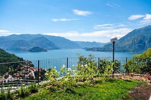 A scenic view of a lake with mountains in the background, a metal fence, and a street lamp. - Vista d'Oro Ulivo Apt. 7 (Perledo)