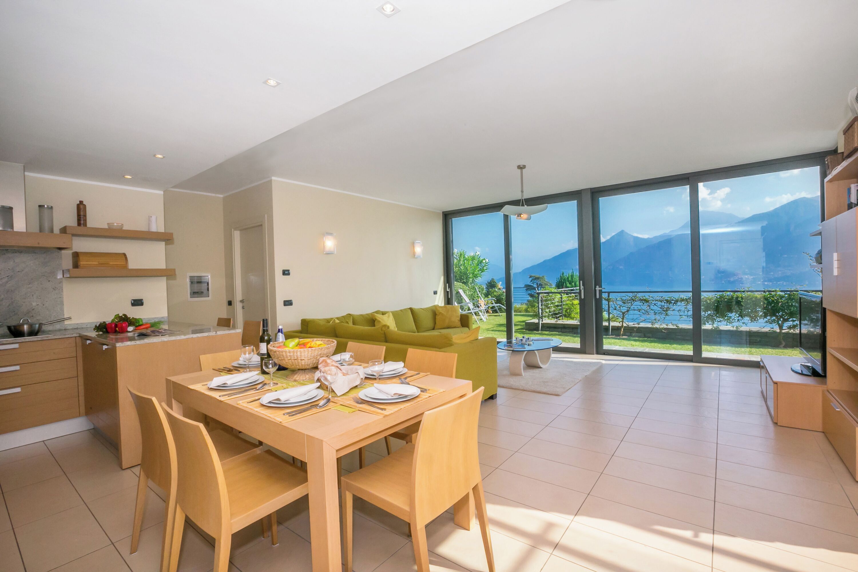 Eine moderne Küche mit Essbereich, großen Fenstern und Blick auf die Berge, sowie ein grünes Sofa.