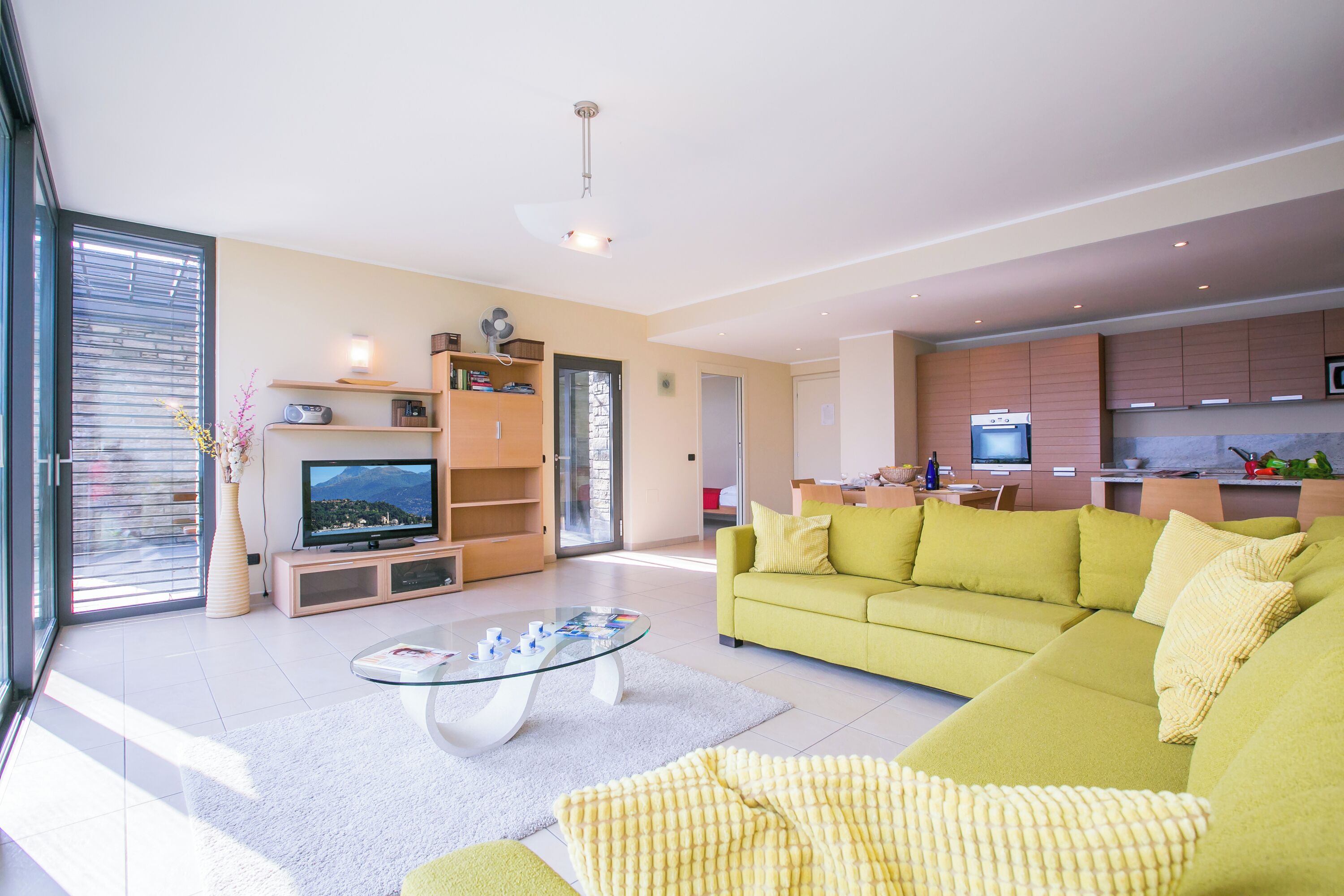 A modern living room with a green sofa, a glass coffee table, and a TV.