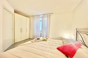 A bedroom with a bed, a bedside table with a lamp, a wardrobe, and a window with curtains. - Menaggio Fantastico (Menaggio)