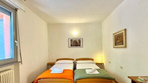 A room with two wooden beds, a window, a radiator, a wall-mounted light, and a framed picture. - Gaeta Splendid Lake (San Siro)