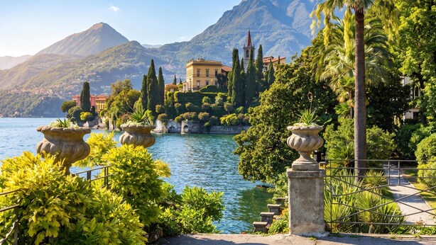 A lakeside property with a mountain backdrop, featuring a building with a bell tower, surrounded by lush greenery and stone structures. - Vista d'Oro Palma Apt. 21 (Perledo)