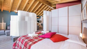 A modern hotel room with a wooden ceiling, a large bed with a red and white checkered bedspread, white linens, and a red pillow. There is a large window with white curtains, a wooden bench, and a small table with a vase of flowers. - Vista d'Oro Palma Apt. 21 (Perledo)