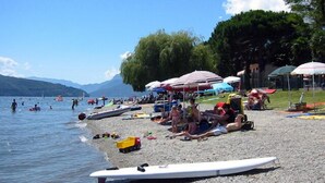 A beach with people, boats, and umbrellas. - Vista Prima (Pianello del Lario)