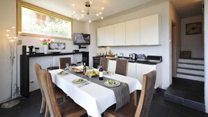 A dining area with a table set for four, a chandelier, and a view of the kitchen. - Vista Prima (Pianello del Lario)