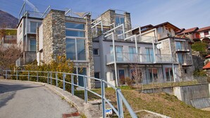 A modern building with stone and glass facades, balconies, and a metal railing along the street. - Vista Prima (Pianello del Lario)