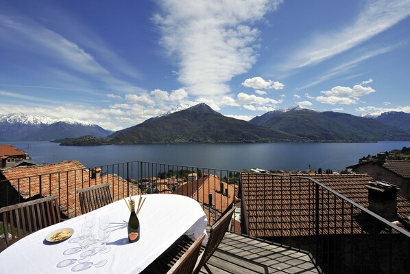 A terrace with a table set for dining, overlooking a lake and mountains. - Vista Prima (Pianello del Lario)