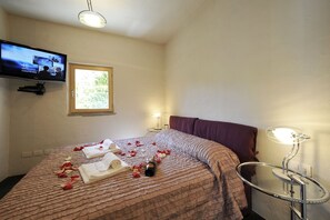 A hotel room with a bed, a TV mounted on the wall, a bedside table with a lamp, and a window with natural light. - Vista Prima (Pianello del Lario)
