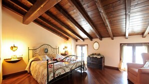 A bedroom with a wooden ceiling, a bed with floral bedding, a nightstand, a dresser, and a chair. - La Piazza Porlezza (Porlezza)