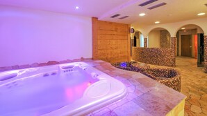 A spa area with a hot tub, stone flooring, wooden paneling, and arched doorways. - Genziana (Livigno)
